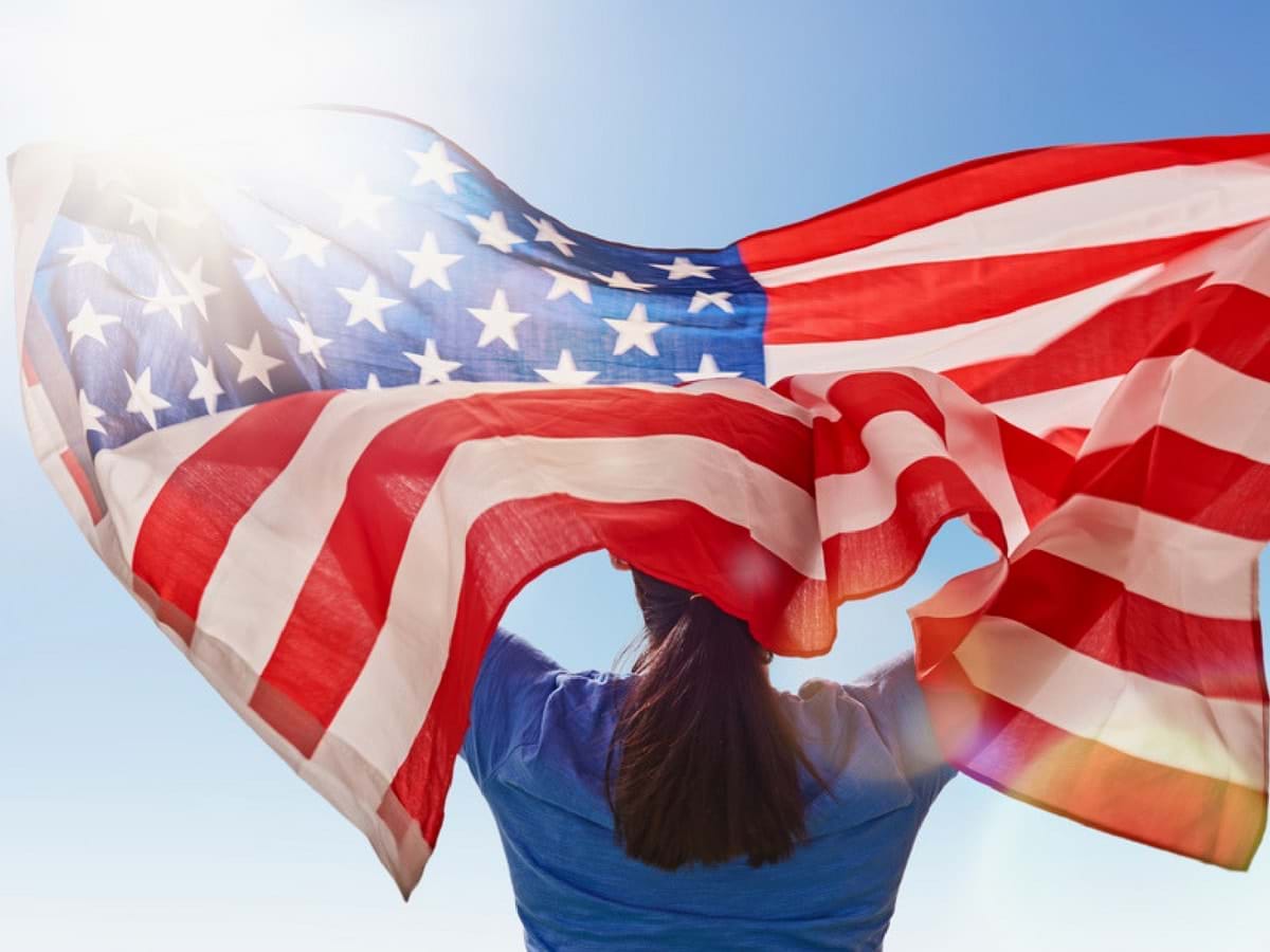 A girl holding an American flag towards a blue sky