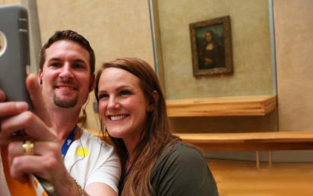 Tourists at the Louvre taking a selfie with the Mona Lisa portrait in the background