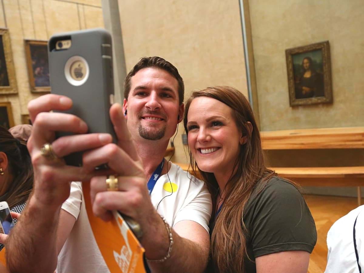 Tourists taking a selfie with Mona Lisa portrait at the back in the Louvre Museum in Paris